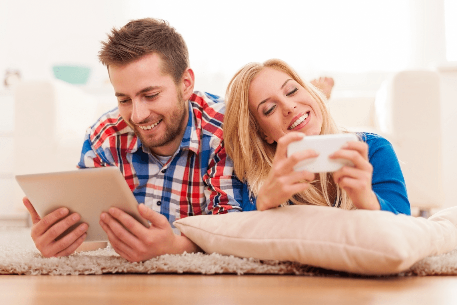 A couple lying on a rug using a tablet and a phone