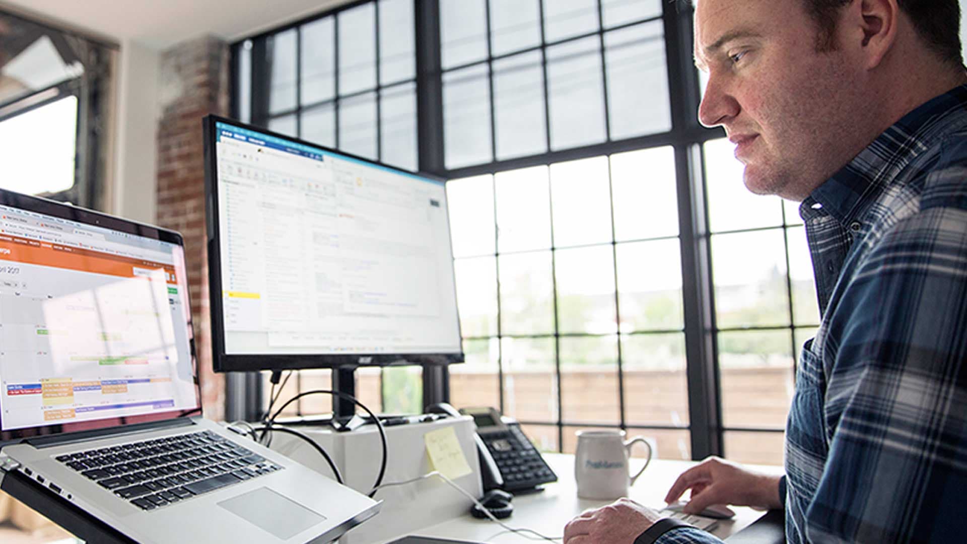 A man working in a CRM across a laptop and a monitor